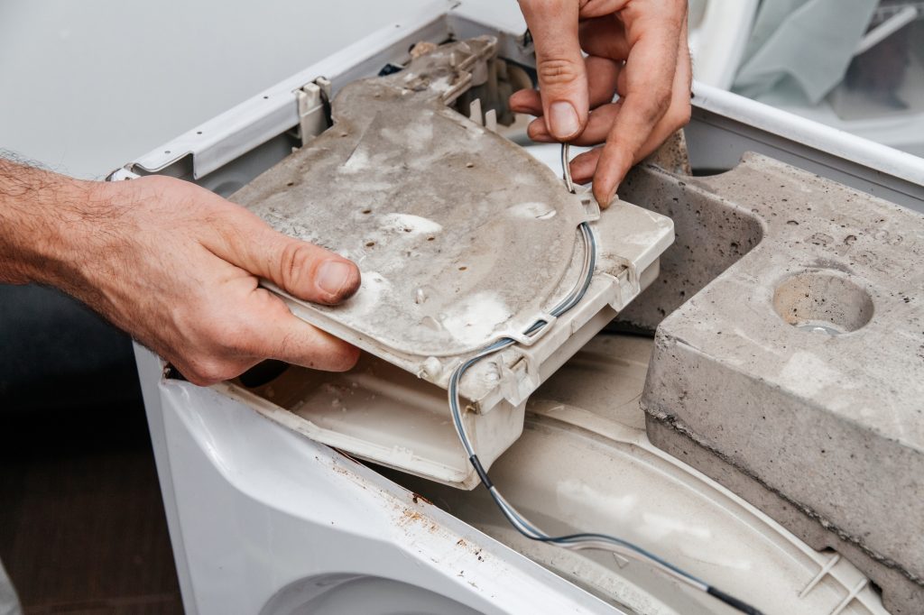 Handyman repairing a washing machine. The hands of a man repair a washing machine.