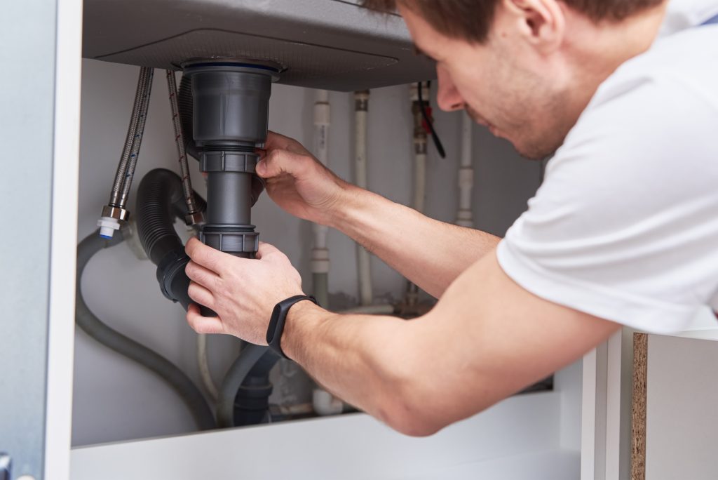 Male plumber repair sink pipe in kitchen