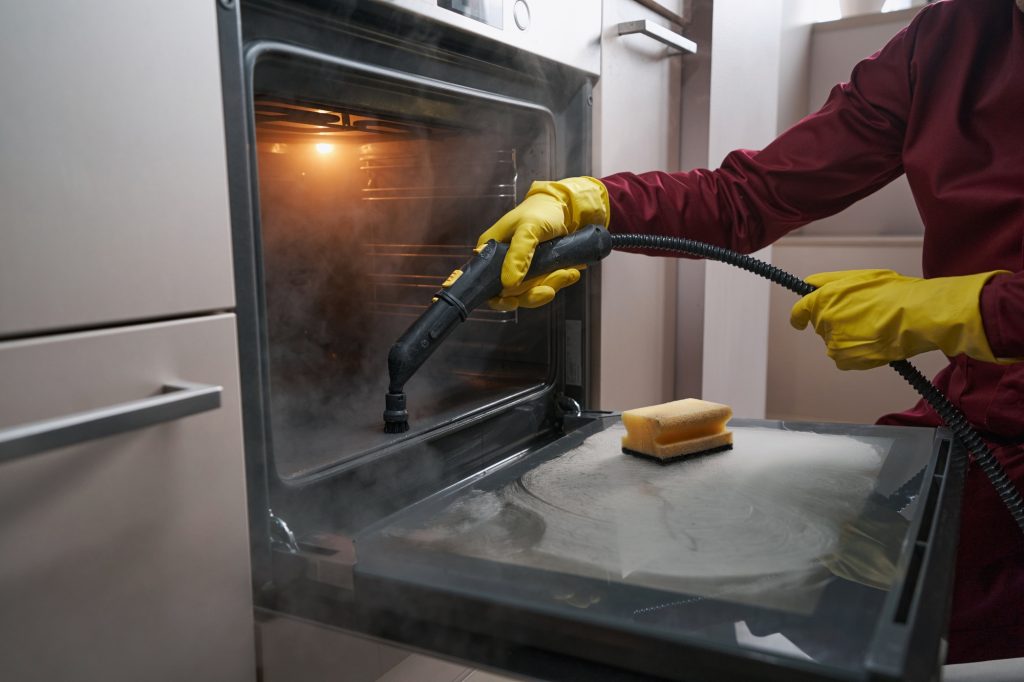 Professional janitor cleaning kitchen appliance with steam