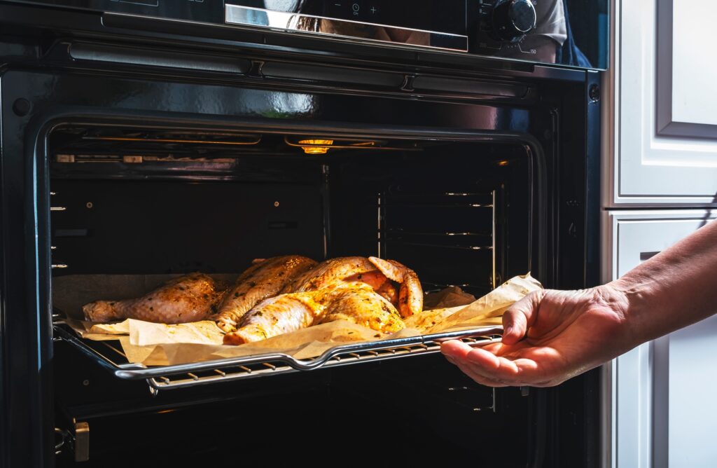 Hand slides baking tray with raw chicken into the oven for baking