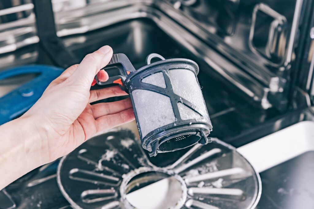 Man cleans the filter in the dishwasher. Maintenance of home appliances.