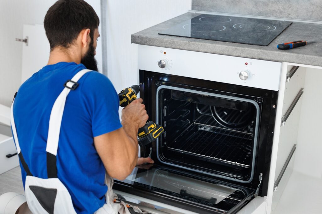 Man installs the oven after assembling the kitchen and screws the bolts with a screwdriver.