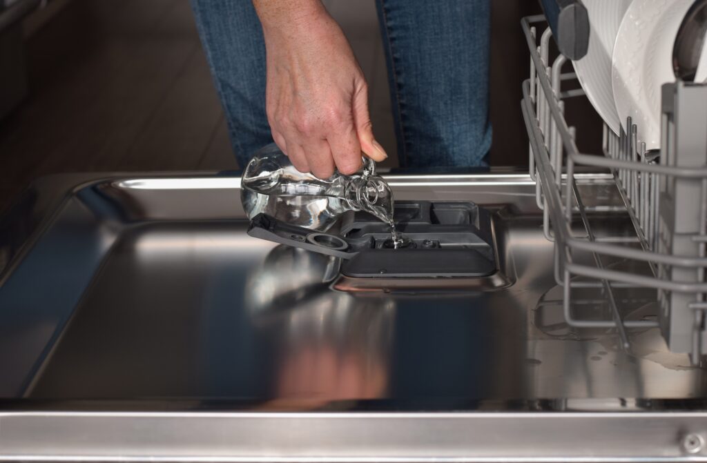 Woman filling up dishwasher rinse aid dispenser with vinegar