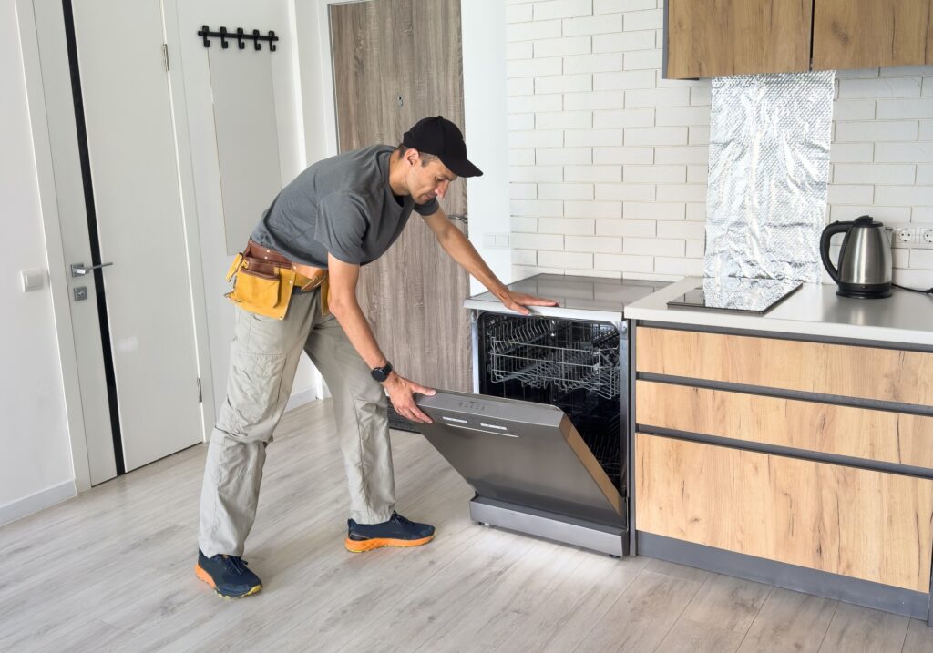 Young Repairman Service Worker Repairing Dishwasher Appliance In Kitchen