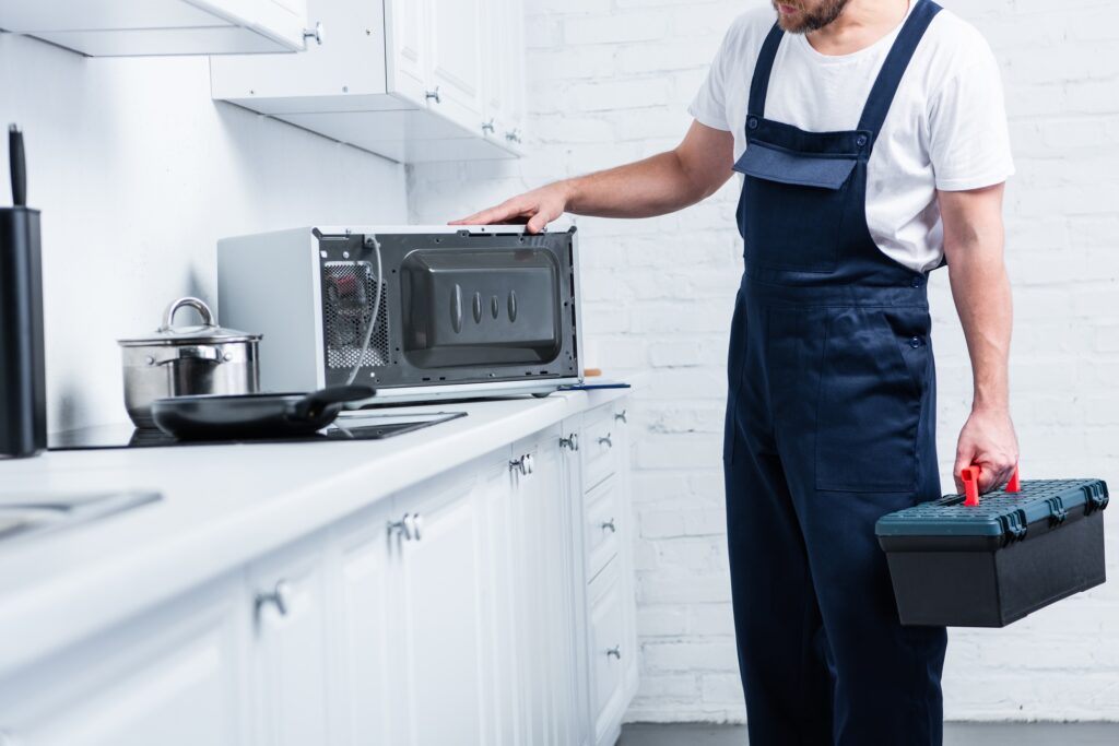 cropped shot of handyman with toolbox checking microwave oven in kitchen