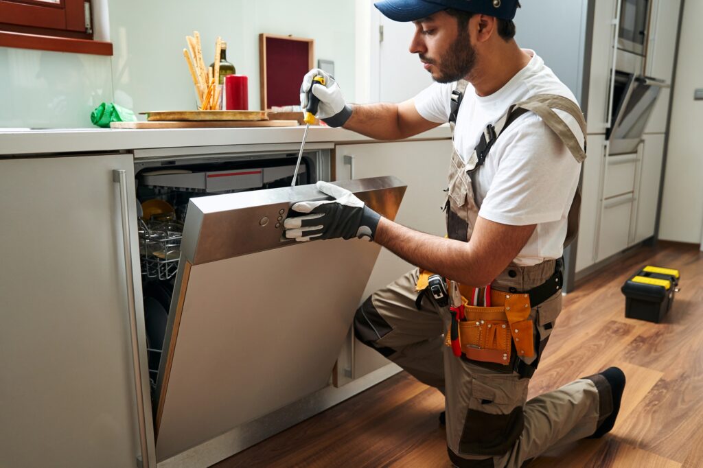 Professional service worker repairing dishwasher appliance in kitchen while use special tools