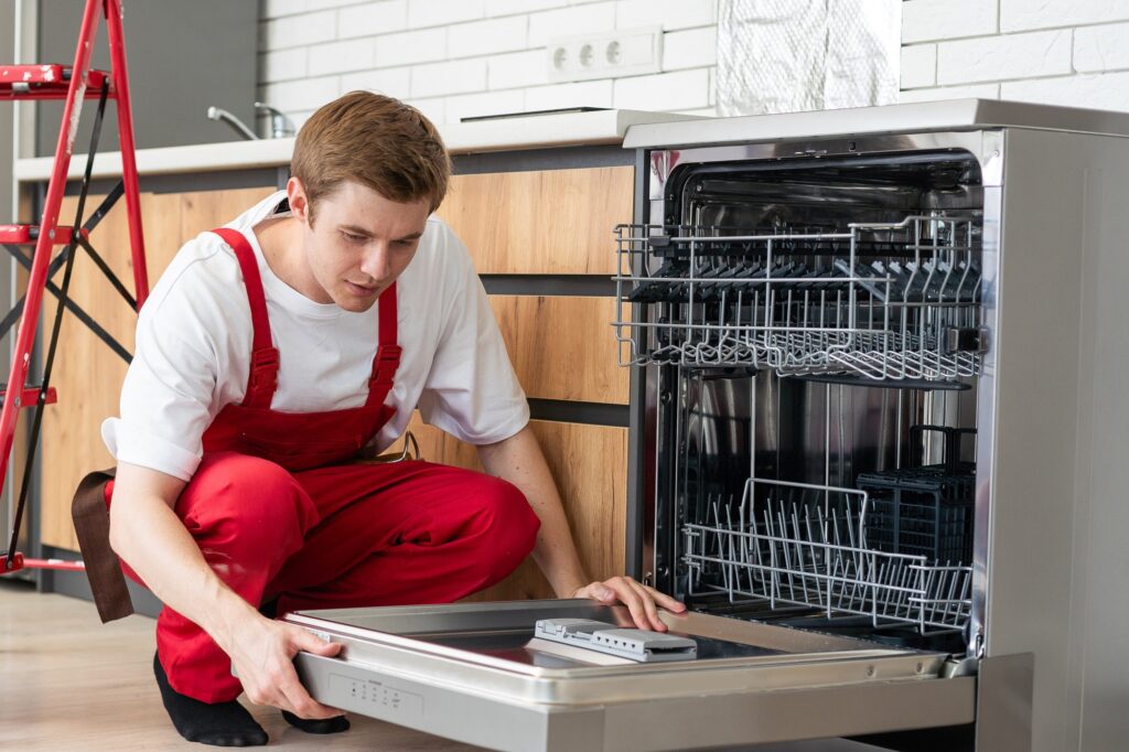 Repair of dishwashers. Repairman repairing dishwasher in kitchen