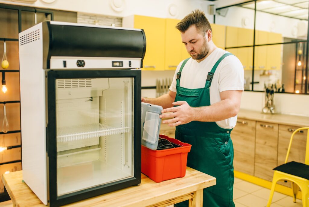 Worker with toolbox repair refrigerator at home