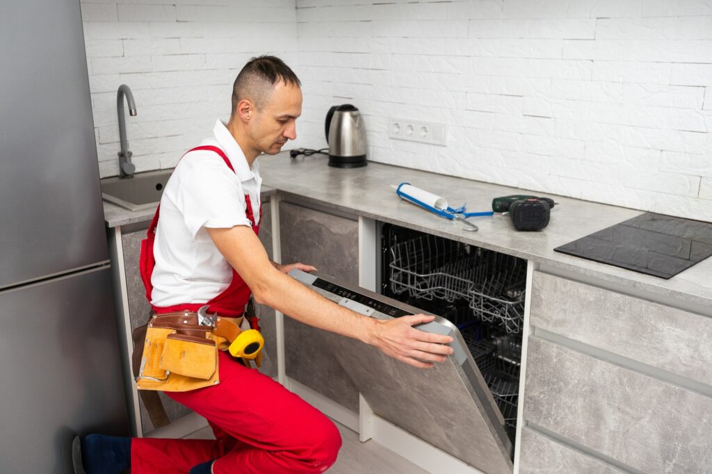 Young Repairman Service Worker Repairing Dishwasher Appliance In Kitchen