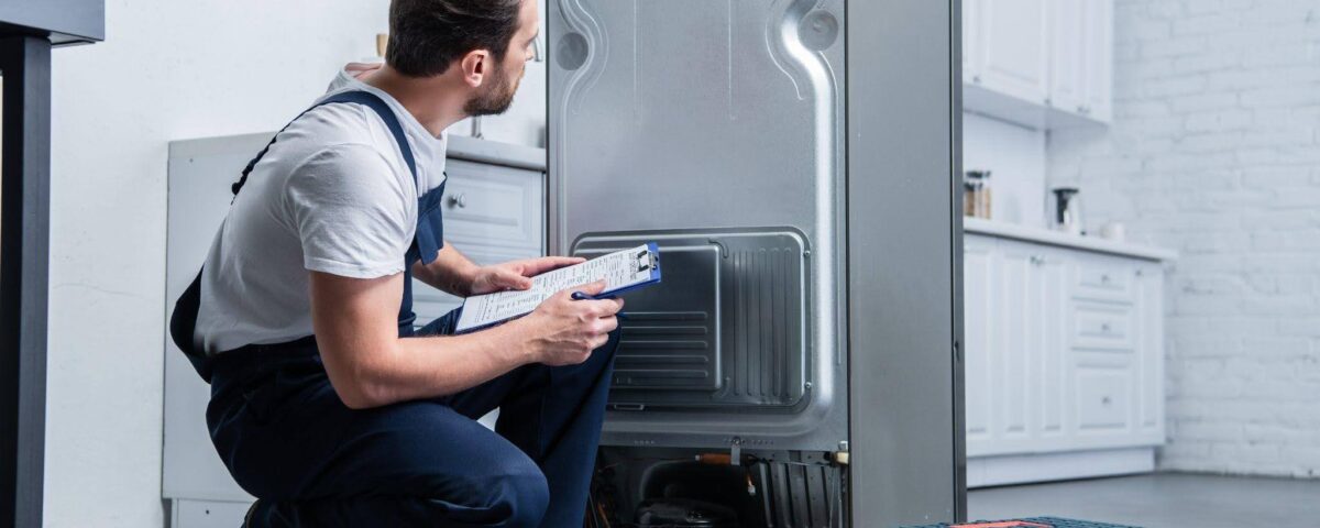A man in a kneeling position next to a refrigerator looking inside with curiosity