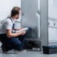A man in a kneeling position next to a refrigerator looking inside with curiosity