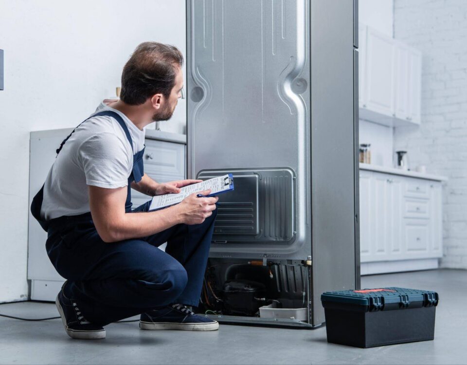A man in a kneeling position next to a refrigerator looking inside with curiosity