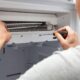 A technician is fixing an air conditioning unit using tools to address the issue