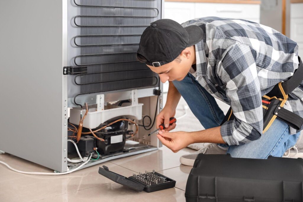 A man works on an appliance repair in a kitchen with tools and utensils visible around him