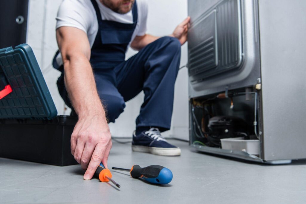 A man repairs an appliance in a modern kitchen surrounded by tools and kitchenware