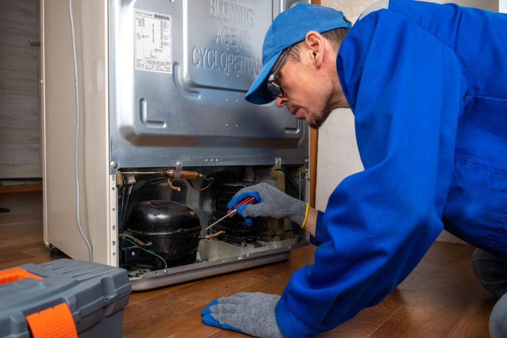 A man wearing a blue shirt and gloves repairs an appliance focused on his task